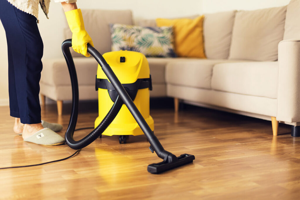Woman cleaning sofa with yellow vacuum cleaner
