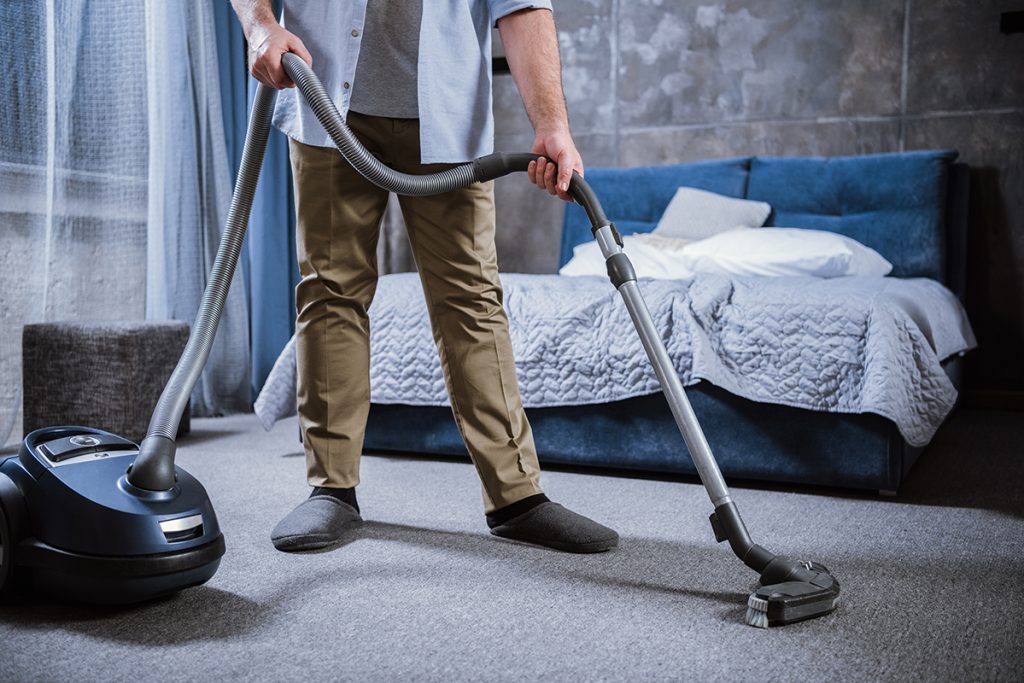 man cleaning and vacuuming bedroom